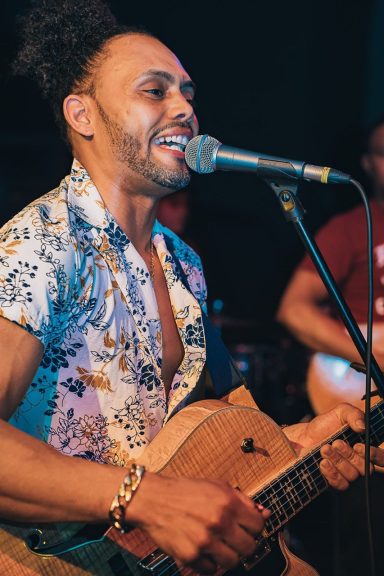 Sandro Reyes cantando y tocando un instrumento musical, con una expresión alegre.